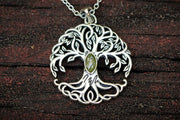 Silver tree of life pendant with a green gemstone on a dark wooden background